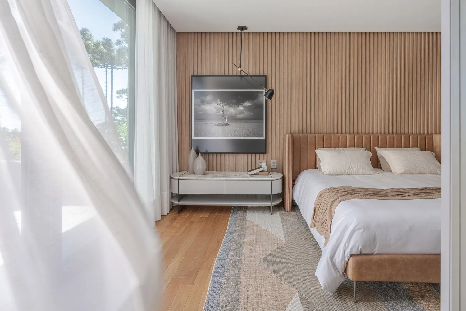 Modern minimalist bedroom with wood accent wall, white bedding, and large windows.