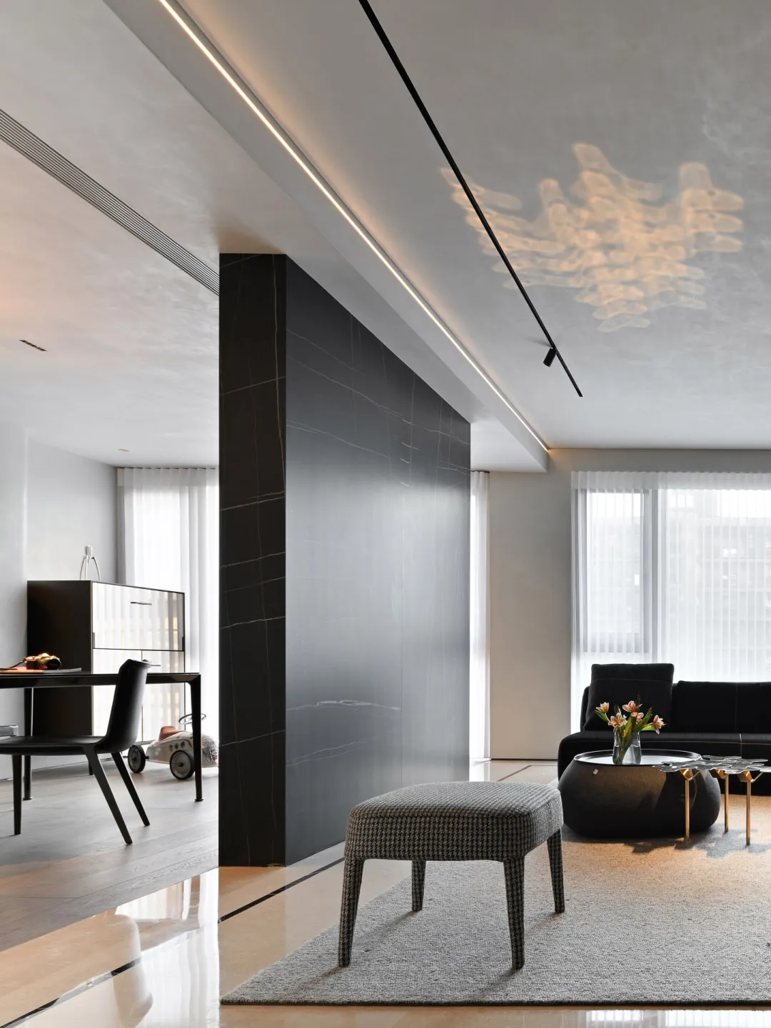 A modern minimalist living room features a large sofa, marble and ceramic surfaces, and a sleek design with dark accents.