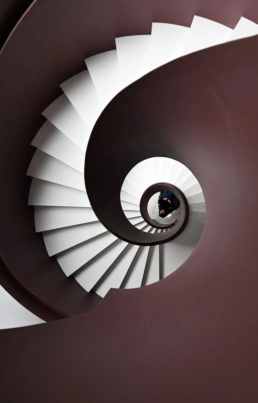 An upward view of a white spiral staircase with concrete steps and walls.