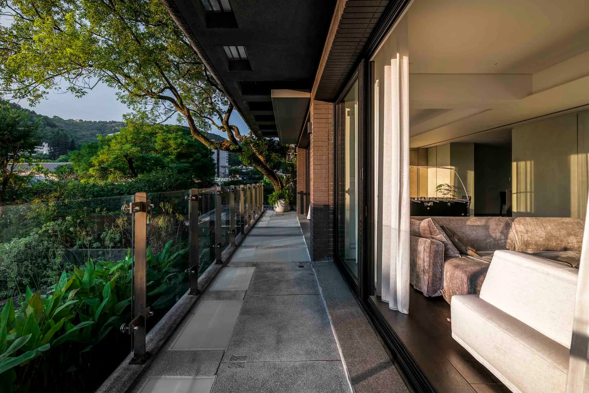 Modern residential balcony with concrete flooring and a view of the greenery, featuring a living room with sofas and a large