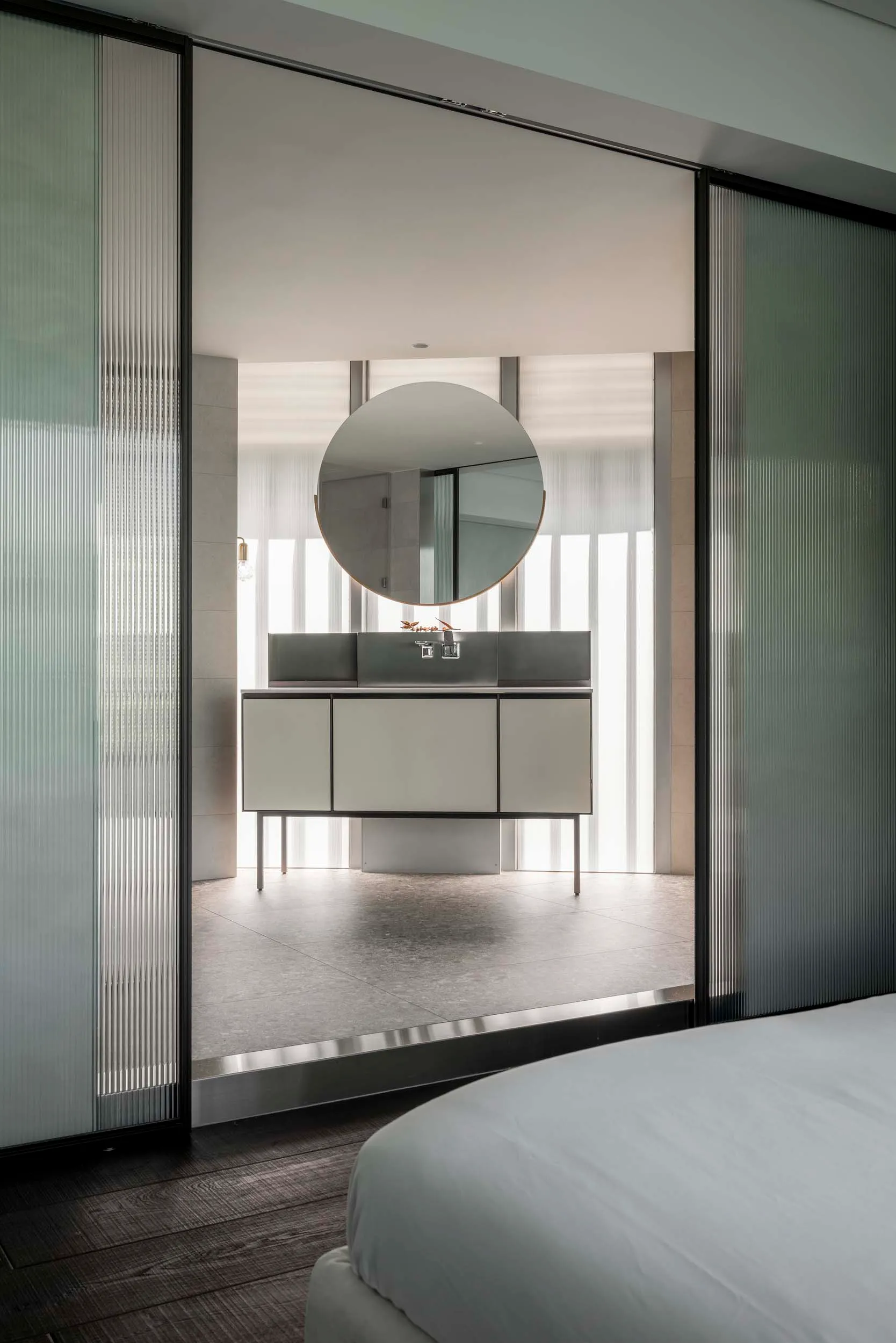 A minimalist bathroom with modern fixtures, including a round mirror and sleek cabinets.