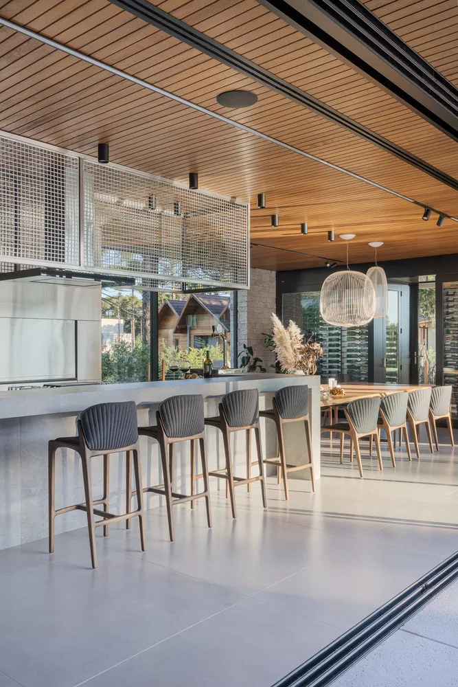 A modern kitchen with a concrete countertop, stainless steel appliances, and high-back upholstered bar stools.