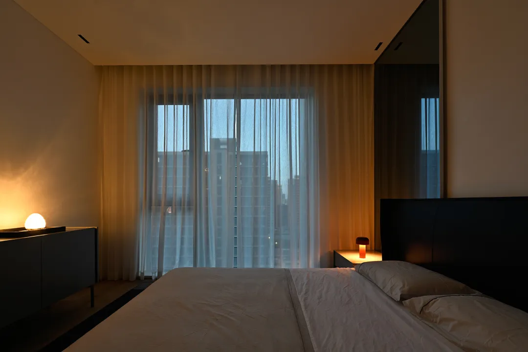 Modern minimalist bedroom with a white bed and cotton blankets, featuring sheer curtains and a city view.