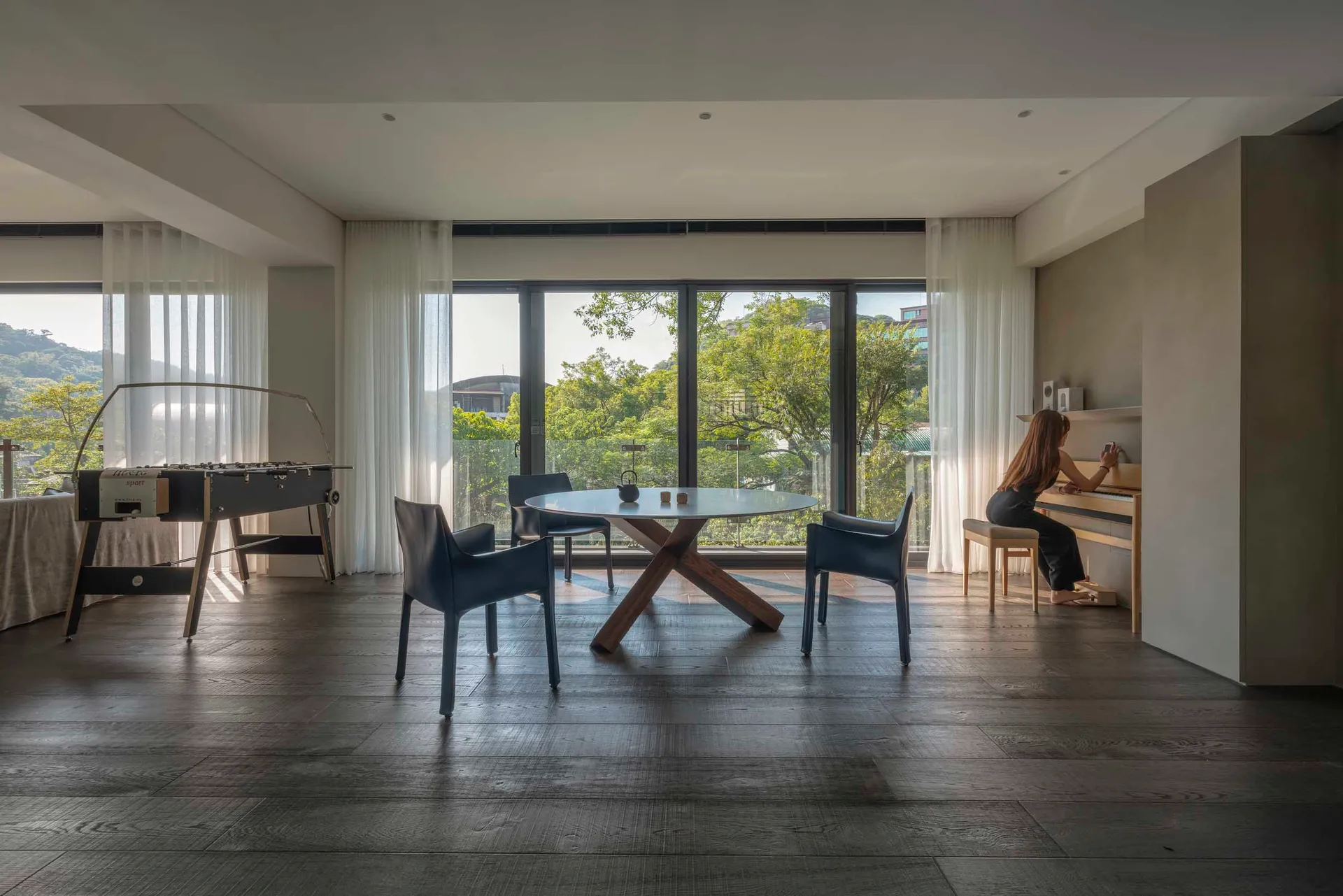 A modern living room in a high-rise residential building with hardwood floors, large windows, and a round dining table with c