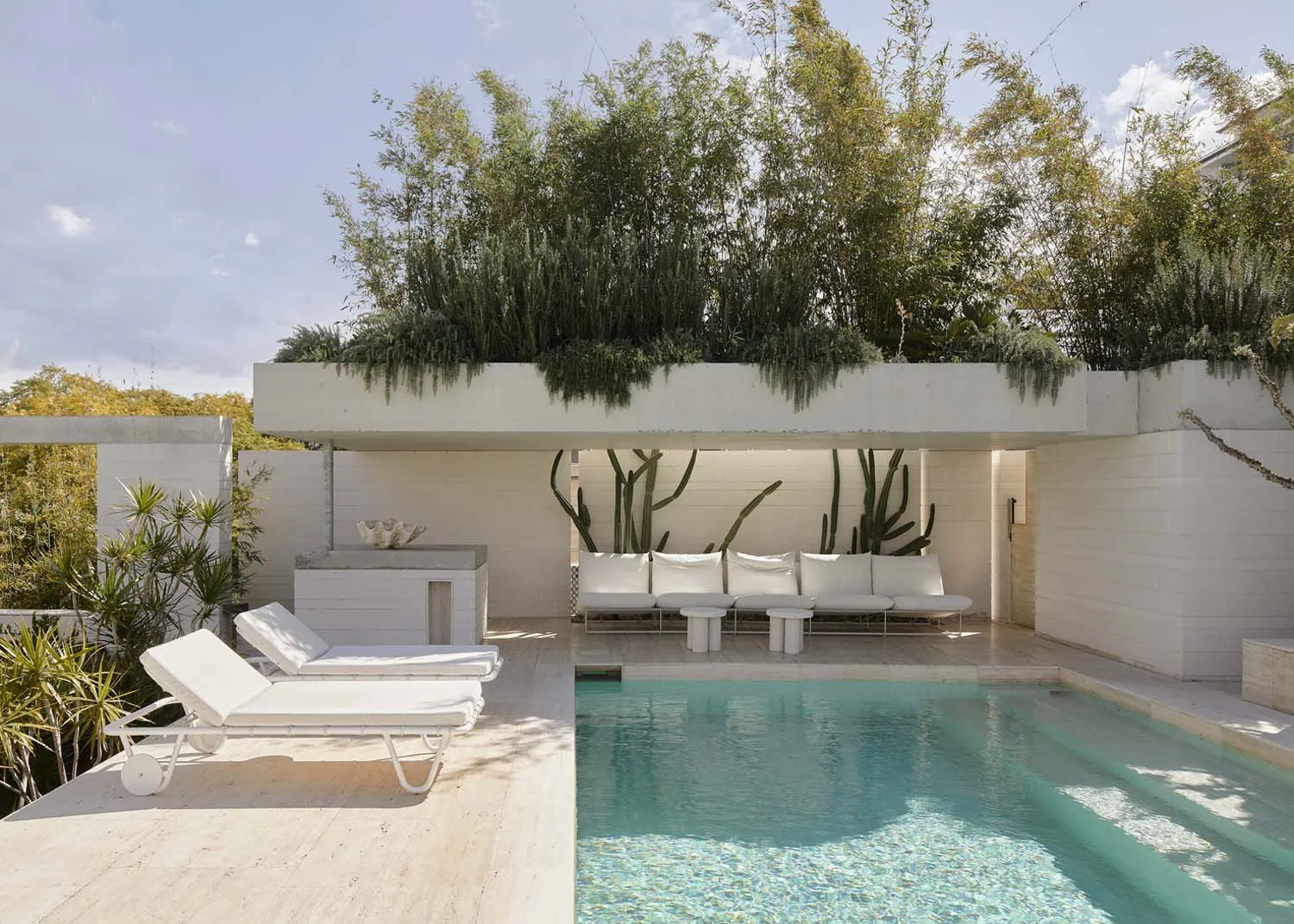 Modern living area with concrete walls and floor, featuring comfortable seating and a serene outdoor pool with greenery.