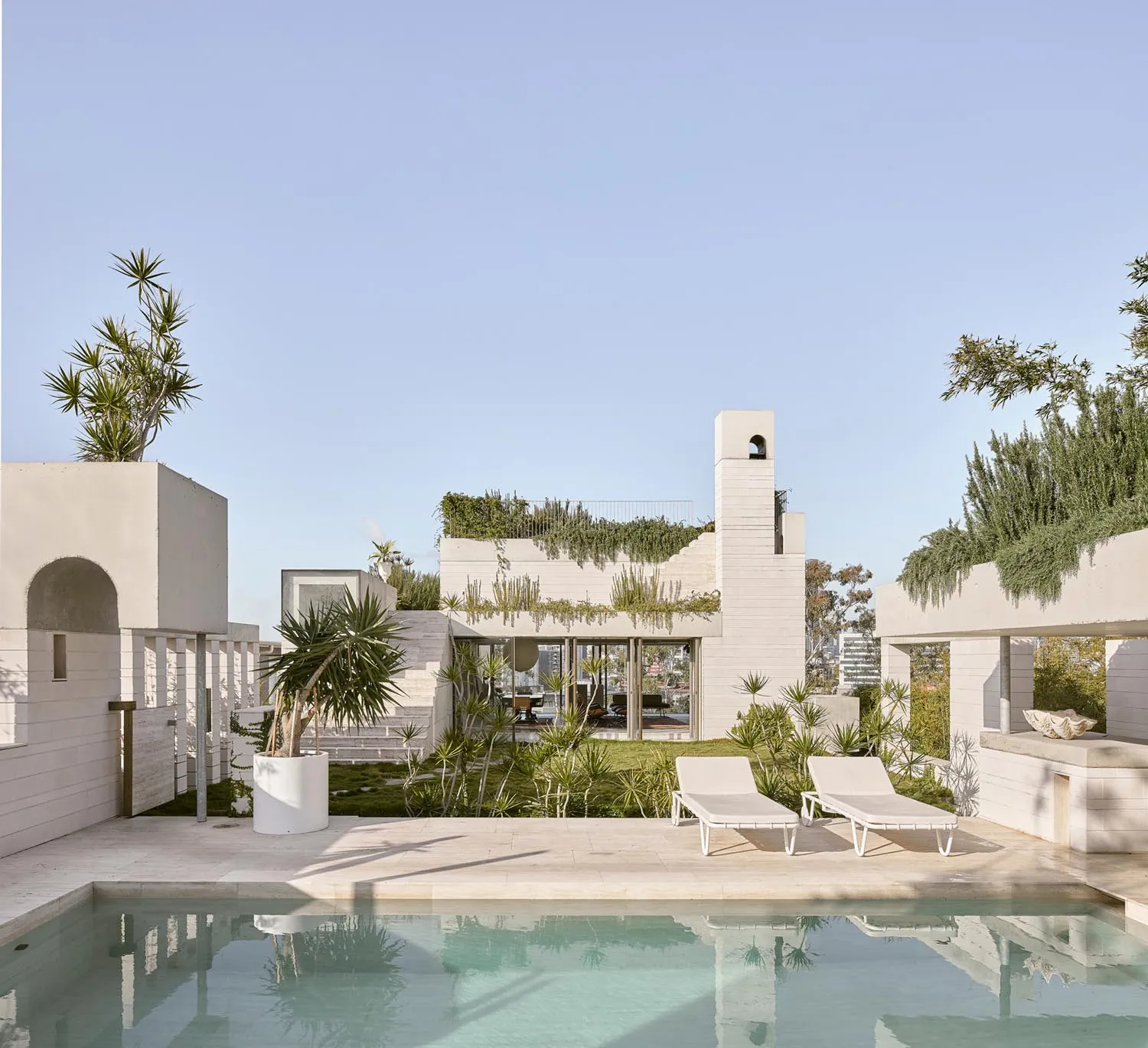 A modern residential backyard featuring a swimming pool, lounge chairs, and greenery on a clear day.