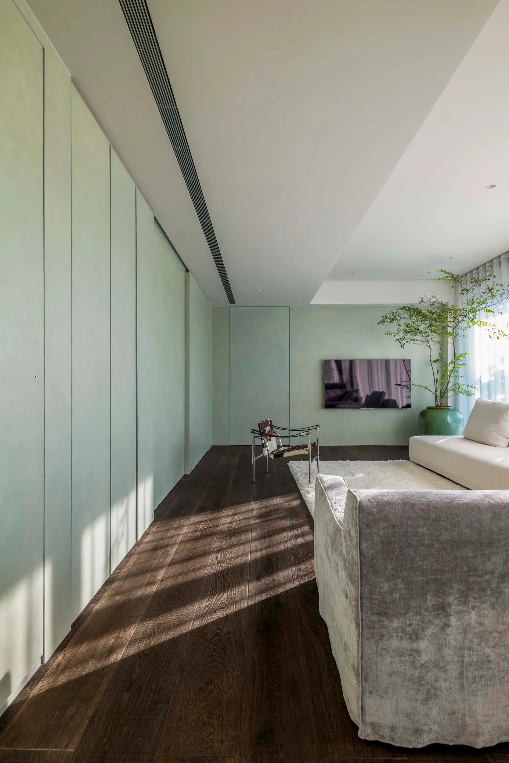 Modern minimalist living room featuring a wooden floor, white furniture, and a large potted plant.