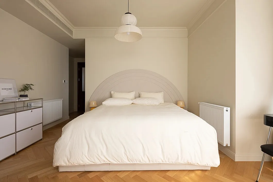 A minimalist bedroom with a bed dressed in neutral-colored bedding and a curved headboard.