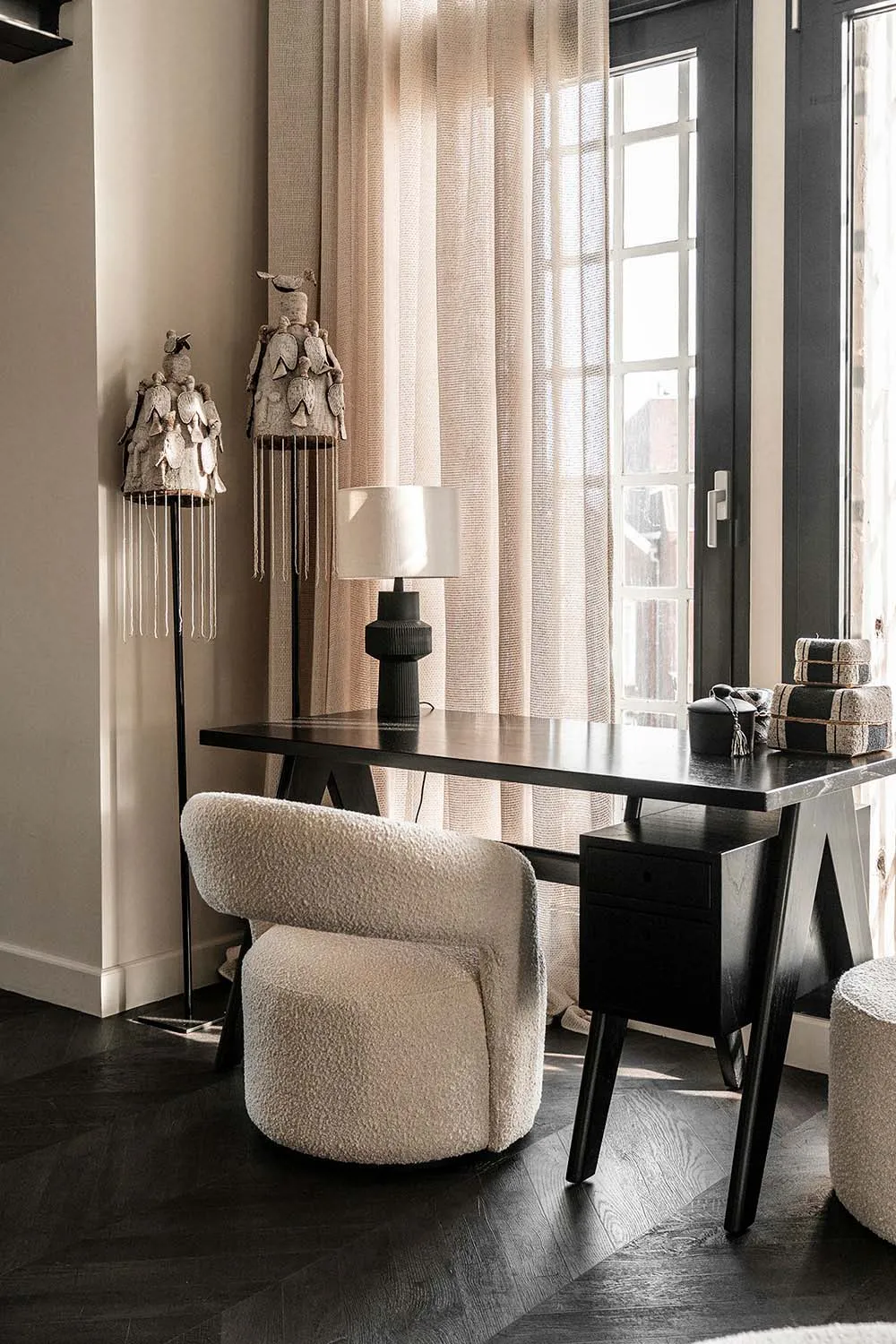 A minimalistic home office featuring a black wooden desk, a white blanket, and curtains by the window.