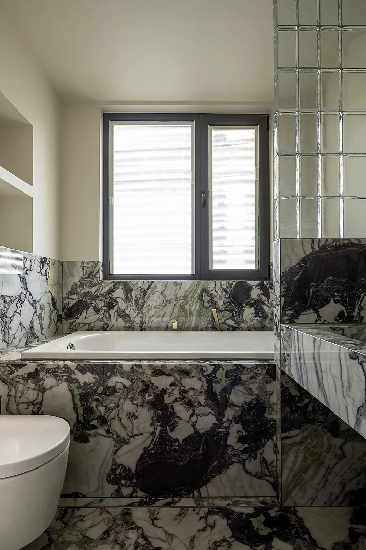 Modern bathroom with white marble fixtures and black accents, featuring a freestanding bathtub and a window with blinds.