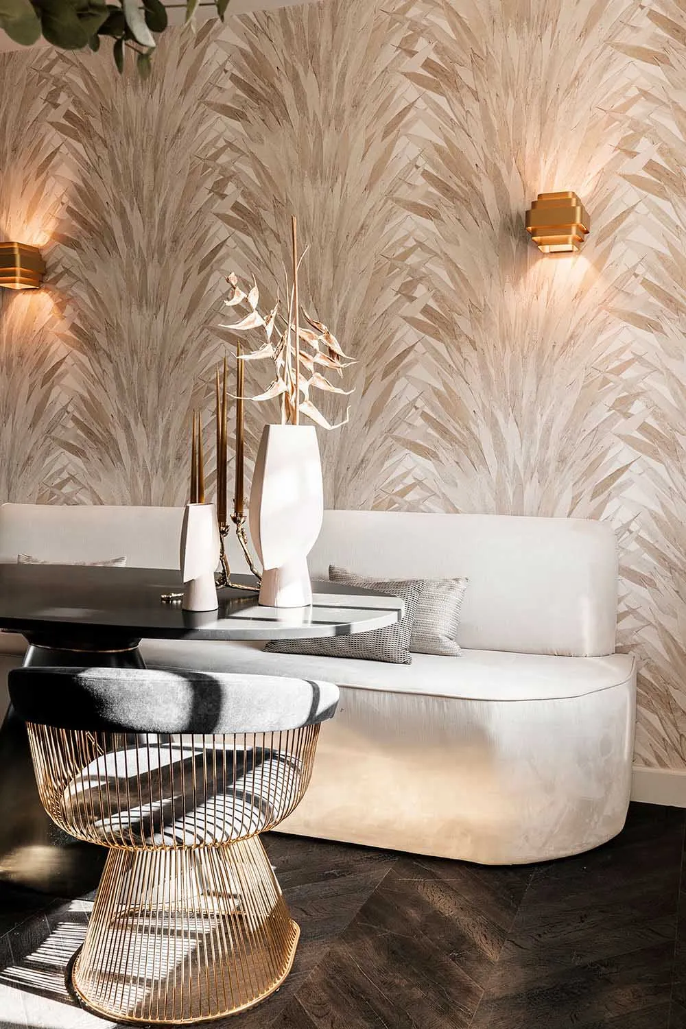 A modern living room featuring a fabric-covered sofa and metallic wire stool with a round table and sconce lighting.