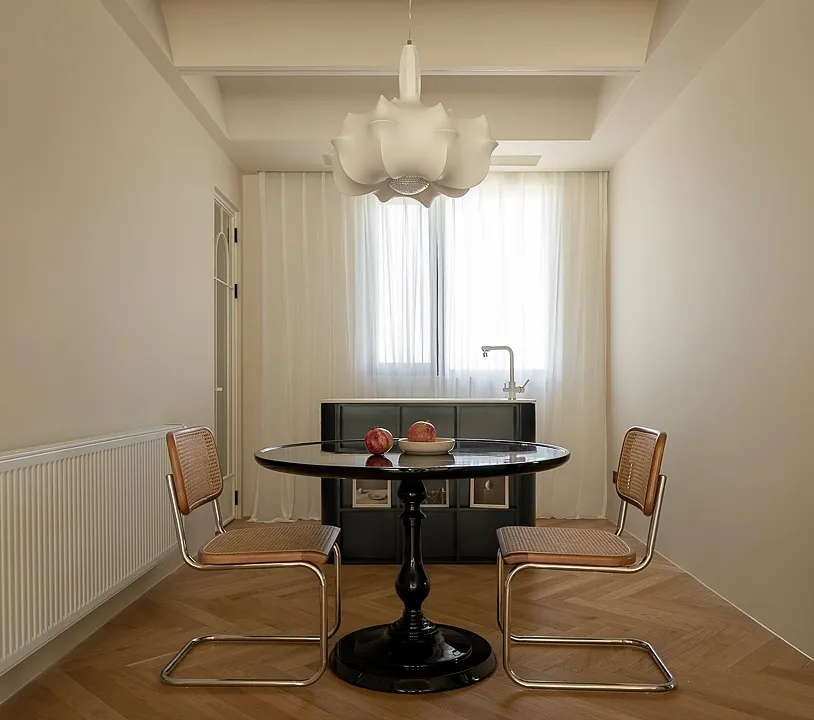 Modern minimalist dining room with black table and leather chairs, glass pendant light, and herringbone wood flooring.