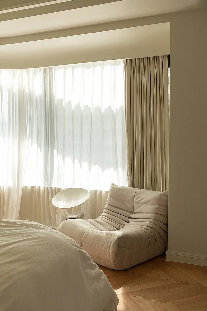 A cozy bedroom with a light-colored bed, white teddy bear, and textured curtains.