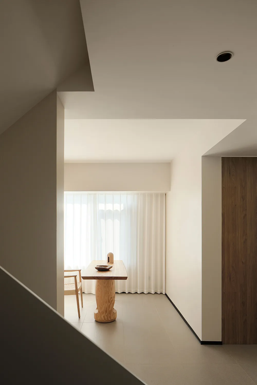 Minimalist residential interior with wooden table and chair in front of window.