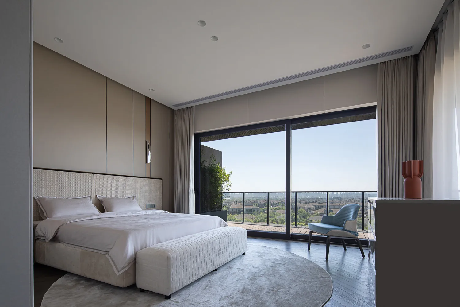 A modern bedroom with a large bed, white bedding, and neutral-colored furniture in a contemporary living space.