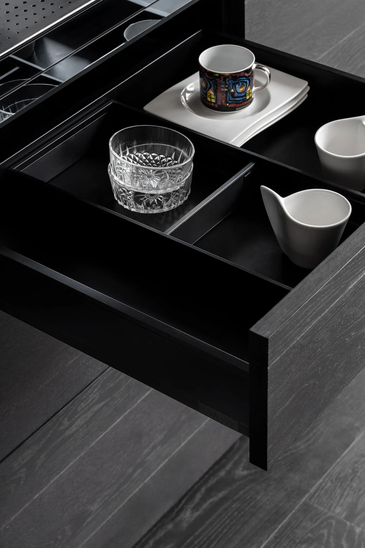 An open kitchen drawer showing black wooden compartments for dishes and cups.