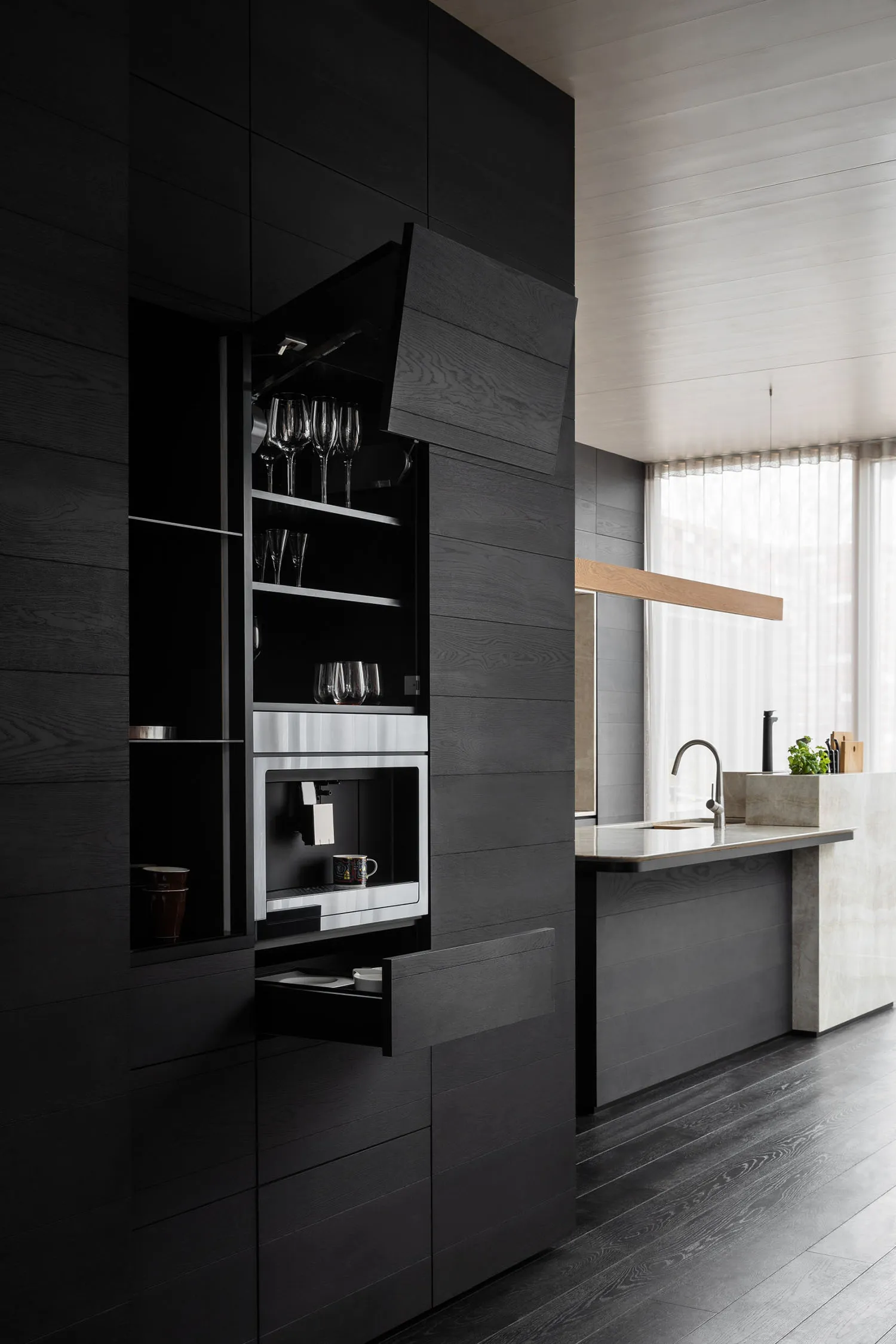 A modern kitchen with black wooden cabinets and metal accents, featuring built-in appliances and a minimalist design.