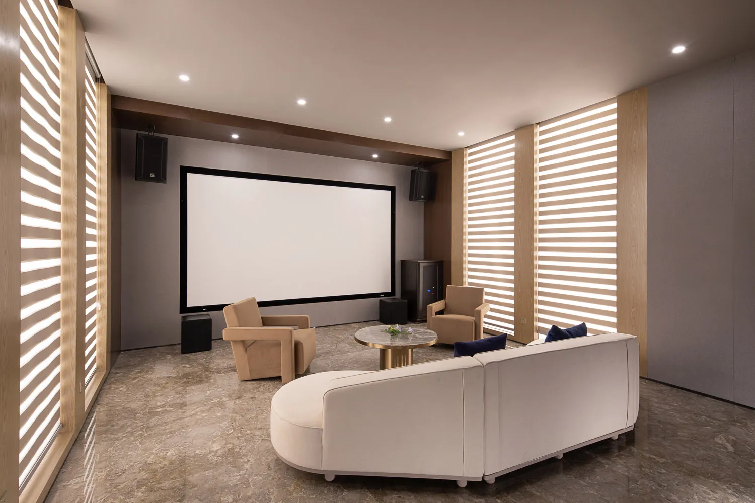 A modern home theater interior with a white screen, beige armchairs, and a white sofa.