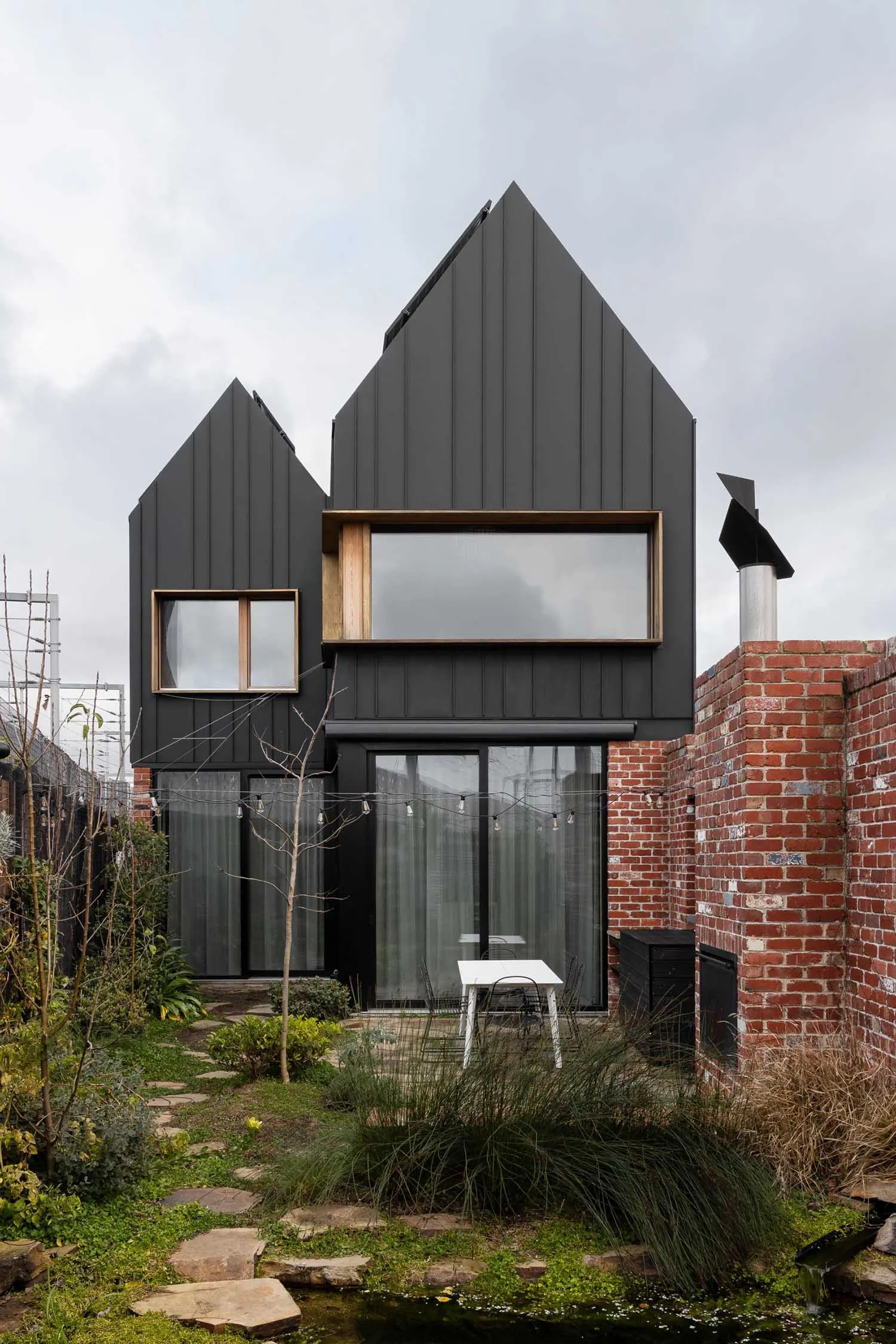 A stylish, modern house exterior with black metal cladding, large windows, and a brick wall.
