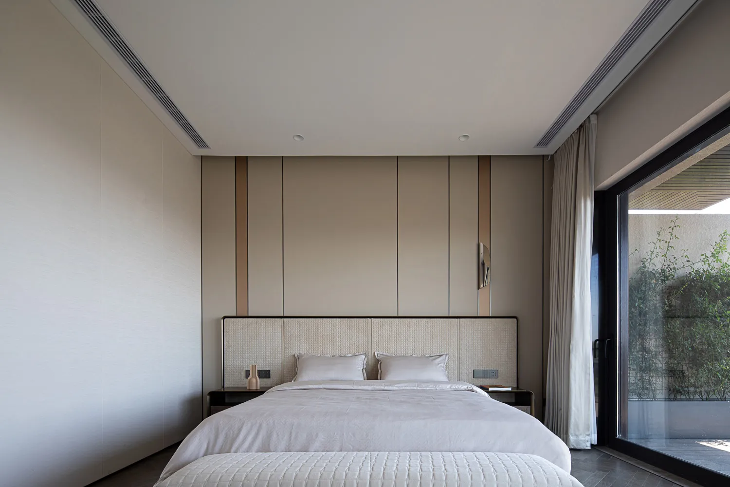 Modern minimalist bedroom featuring neutral-toned furniture and decor, clean lines, and a large window.