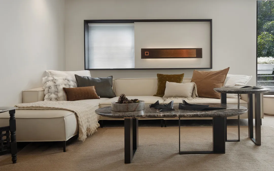 A modern minimalist living room featuring a white sectional couch adorned with a variety of textured throw pillows, a marble