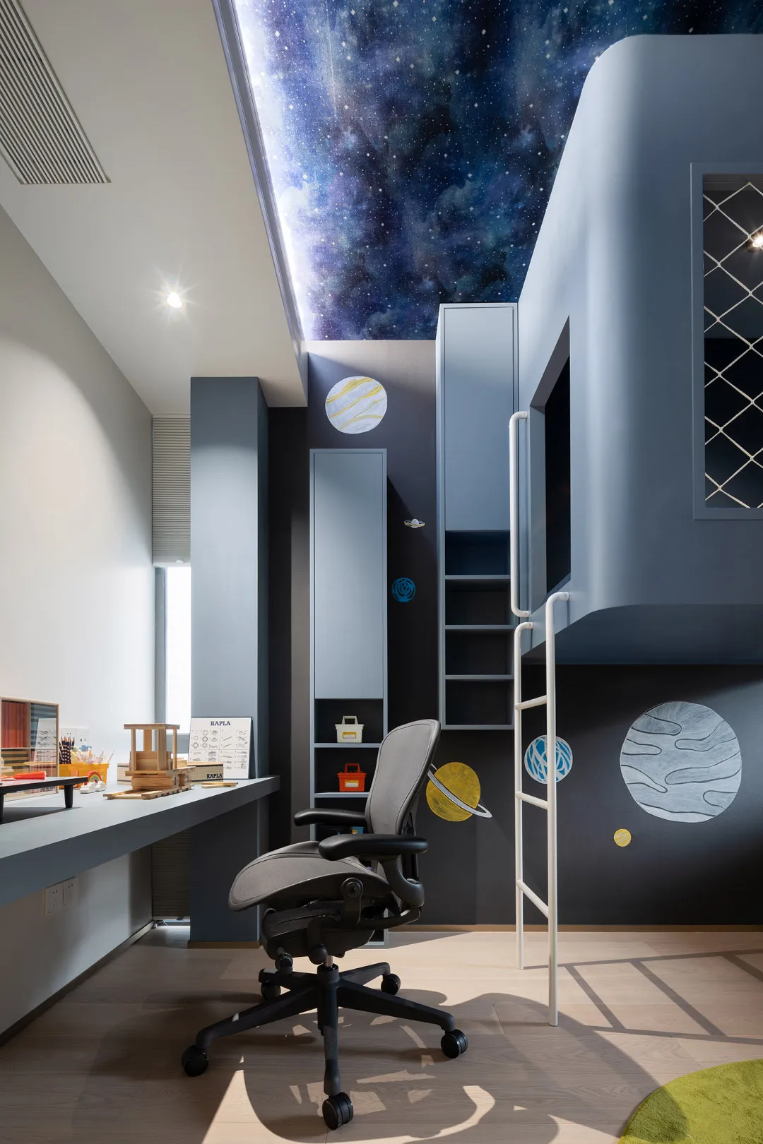 A space-themed children's bedroom with blue, gray, and green colors, featuring a galaxy ceiling and a loft bed with a ladder.