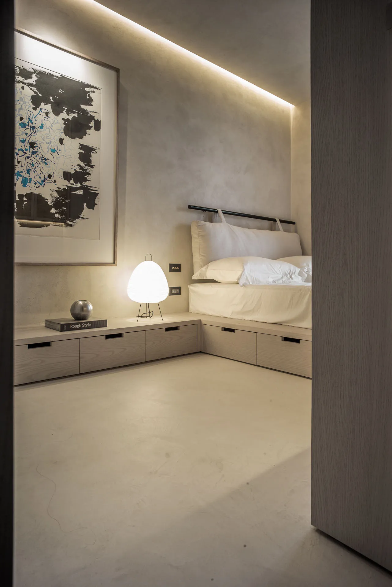 Minimalist bedroom with concrete floor, white bedding, and abstract painting.