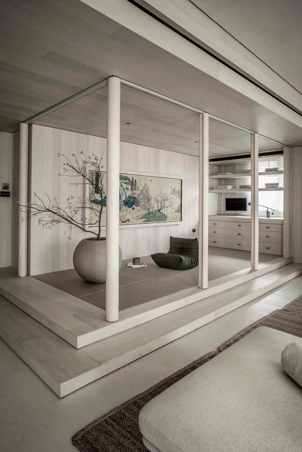 A modern minimalist living room with a Zen pod featuring a potted tree and a framed painting.