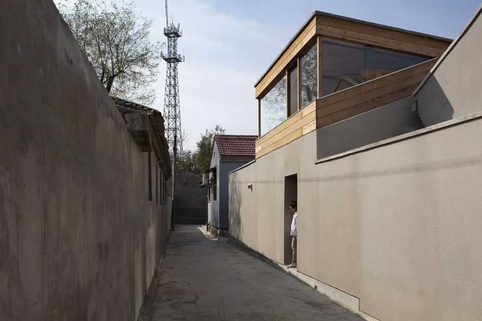 A modern exterior building made of concrete materials with large windows and a metal antenna tower in the background.