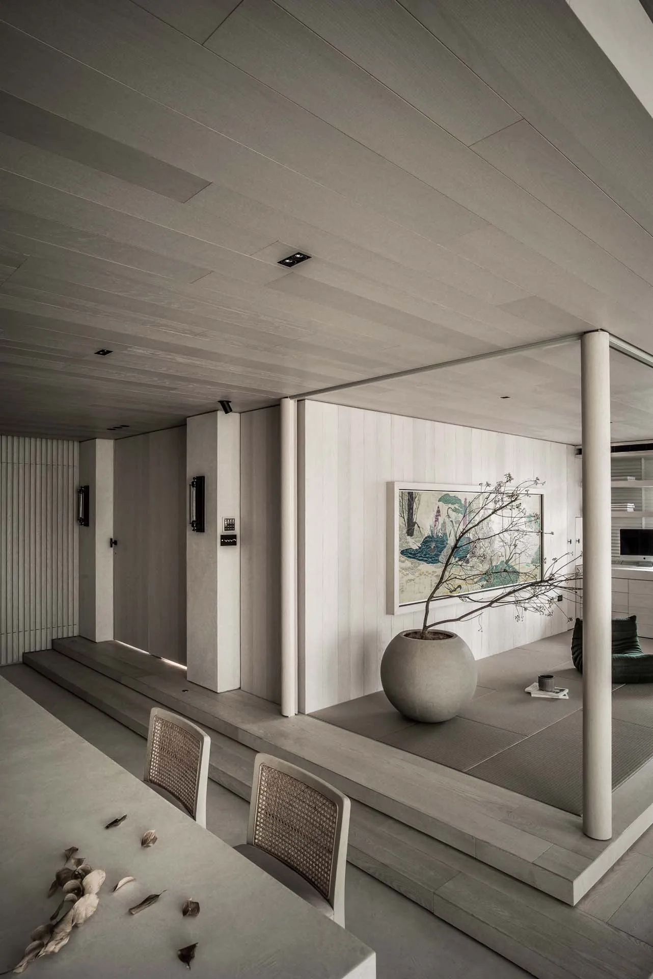 Modern minimalist living room featuring wood flooring and furniture, with a potted plant and abstract painting on the wall.