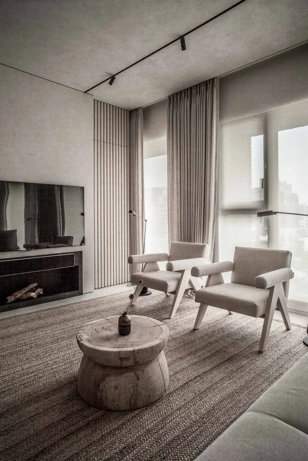 A modern living room with neutral textiles and wooden accents, featuring two armchairs, a coffee table, and a fireplace.