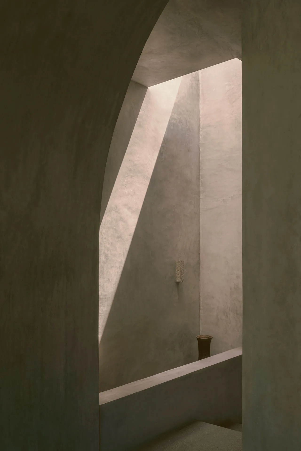 A minimalist interior design featuring concrete walls and a geometric light shaft.