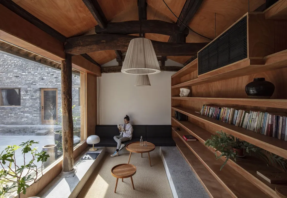 A minimalist library with wooden shelves and a woman reading a book on a black bench seat.