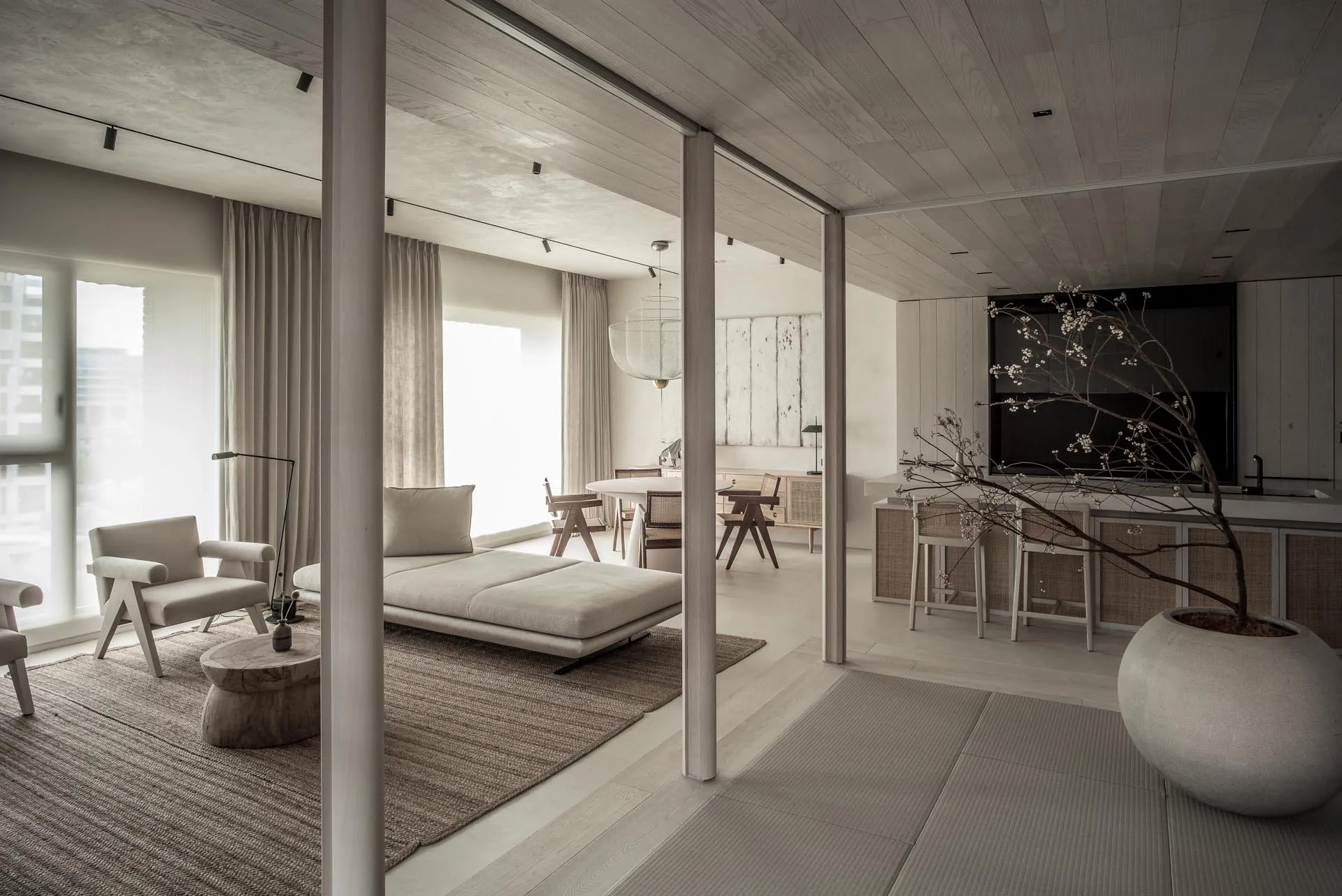 A minimalist living room featuring a white couch, wooden coffee table, and floor-to-ceiling windows, with a decorative tree i