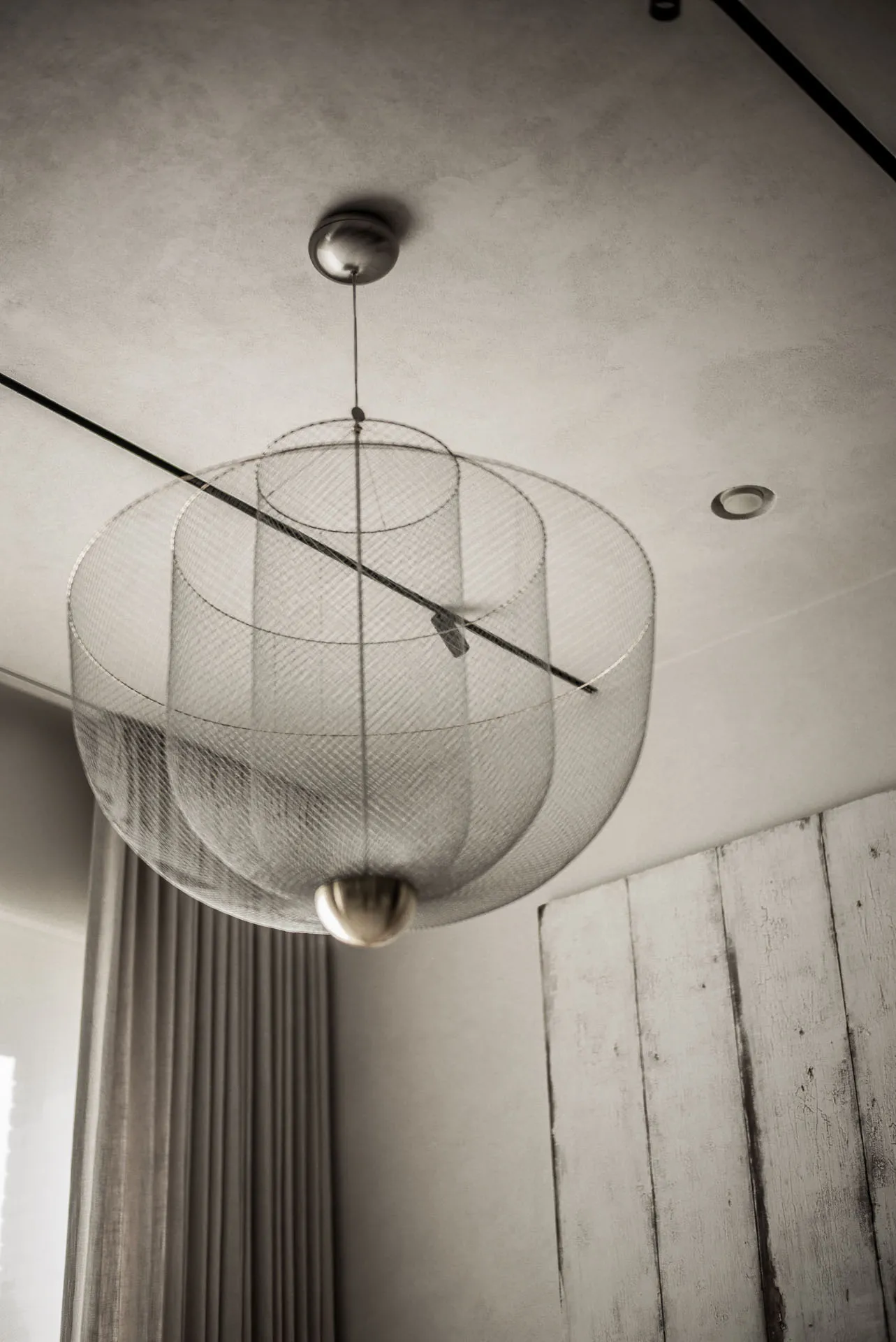 A modern interior with a metal mesh and brass lamp hanging from the ceiling.