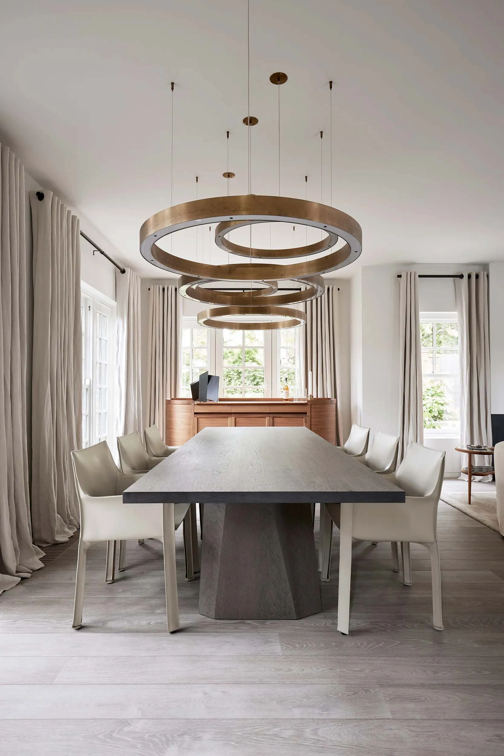 A modern residential dining room with a concrete table and chairs, surrounded by large windows and a minimalist interior desi