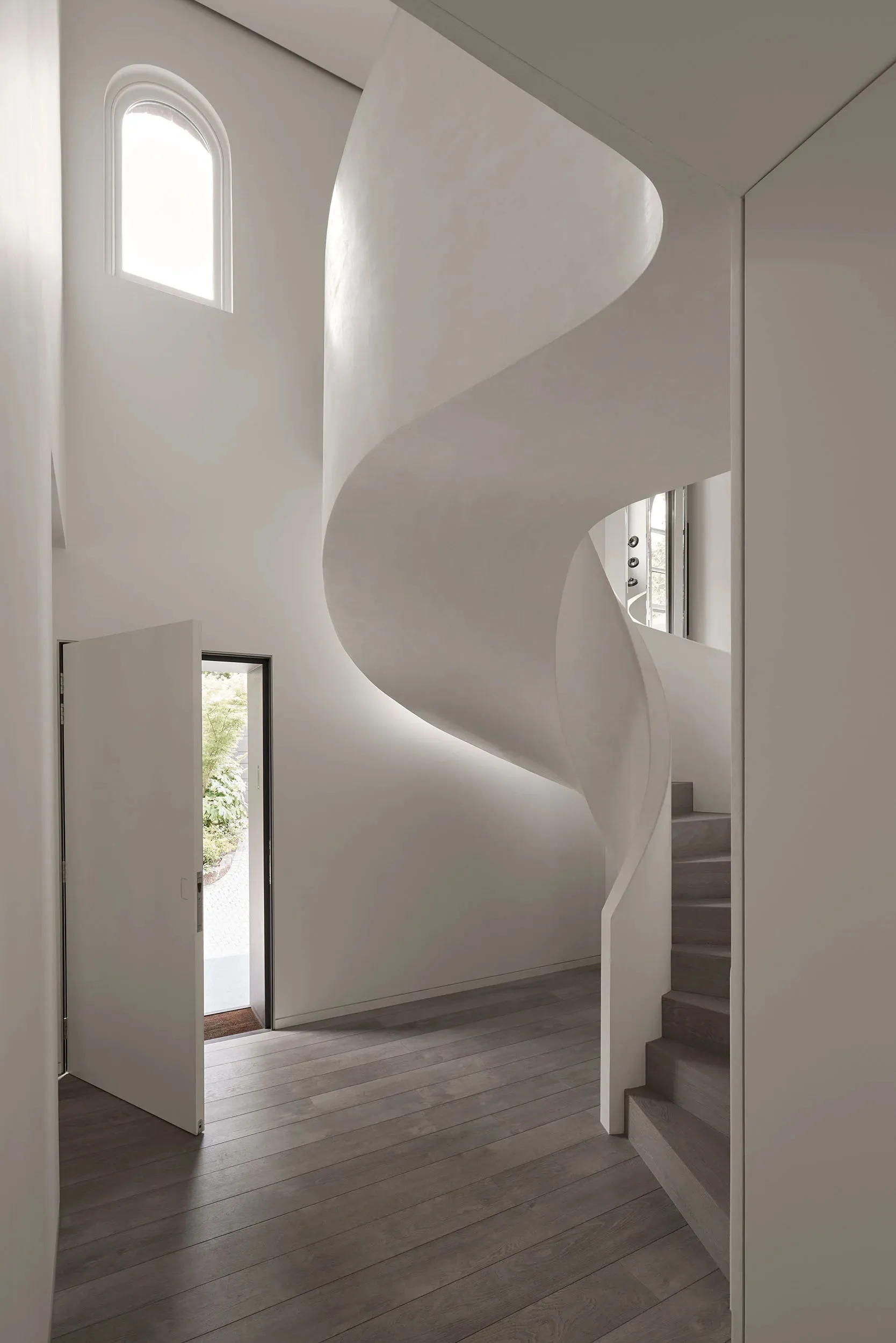 Modern interior design featuring a minimalist concrete staircase with natural light coming through an arched window.