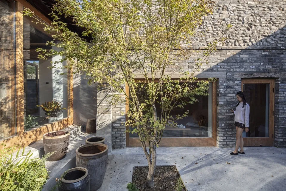 A modern stone house with a courtyard featuring potted plants and a tree.