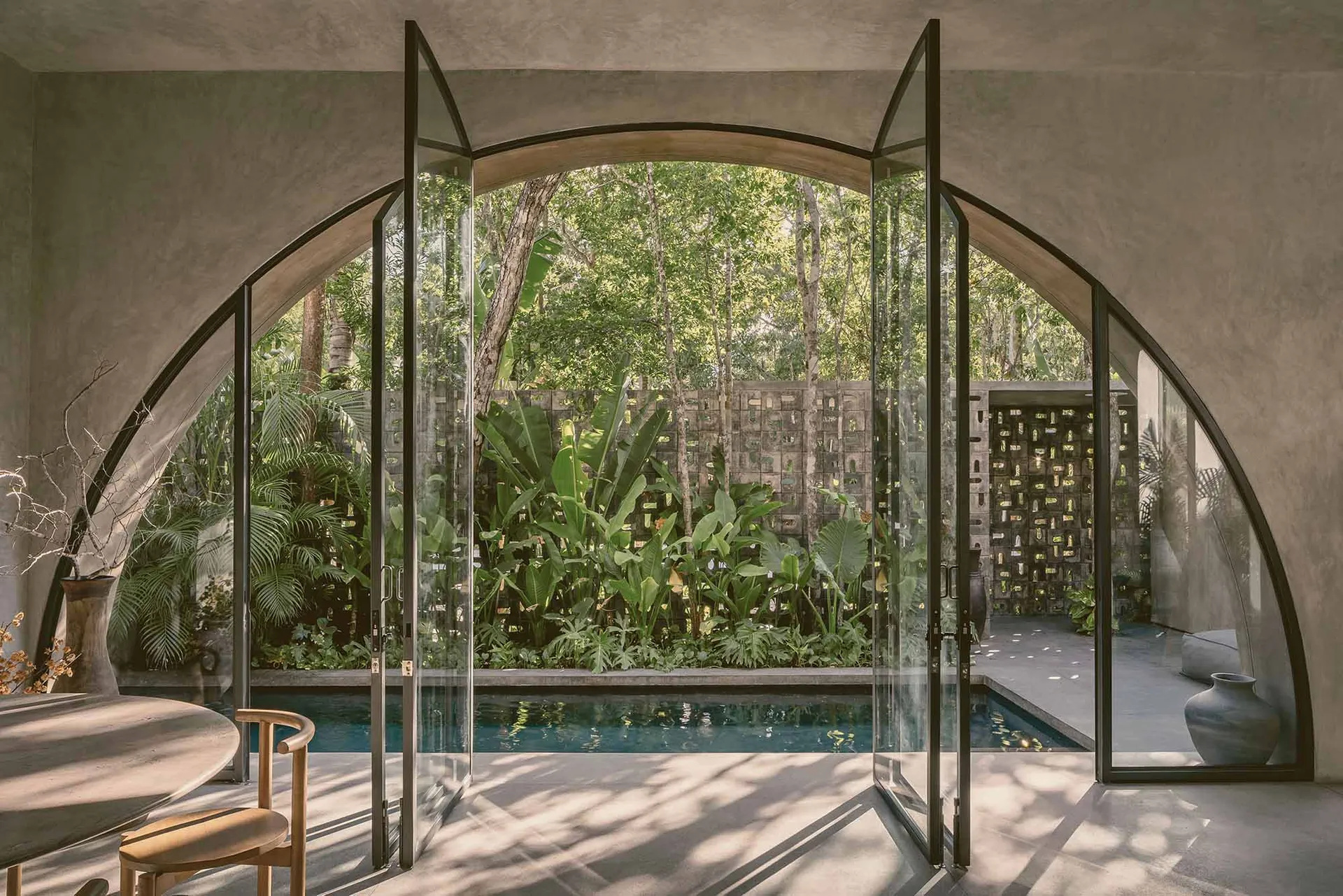 An elegant indoor residential pool surrounded by glass walls with lush greenery outside.