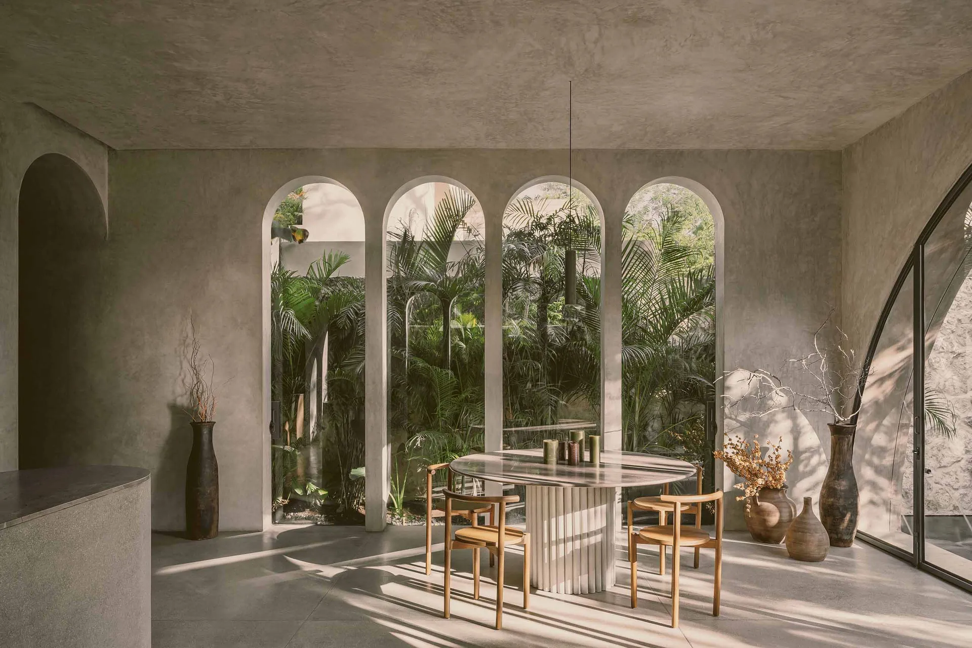 Modern restaurant interior with minimalist design, featuring concrete walls, arched windows, and a glass dining table surroun