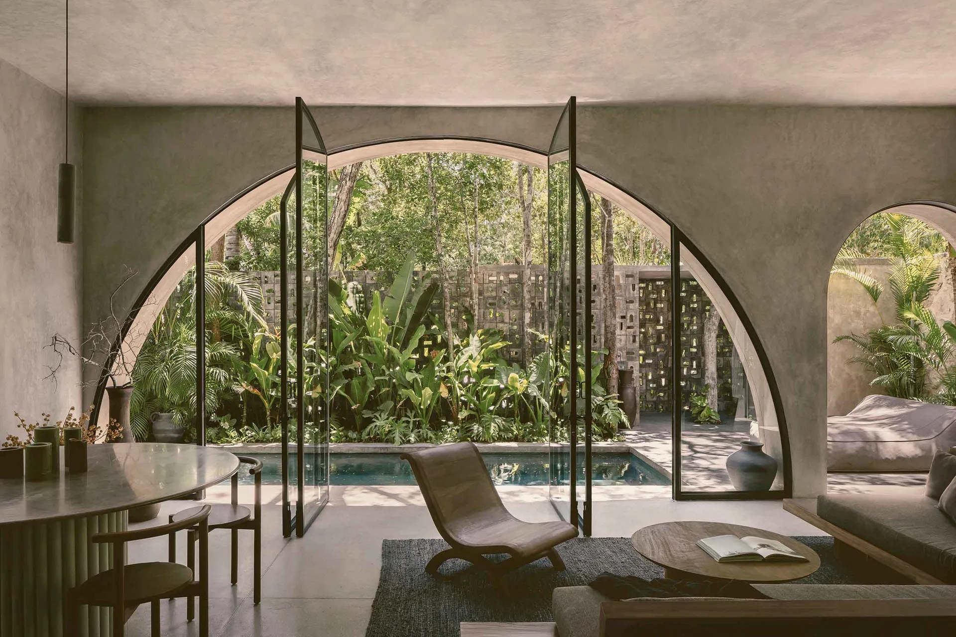 Modern residential interior featuring concrete walls and glass doors with a view of a pool and garden.