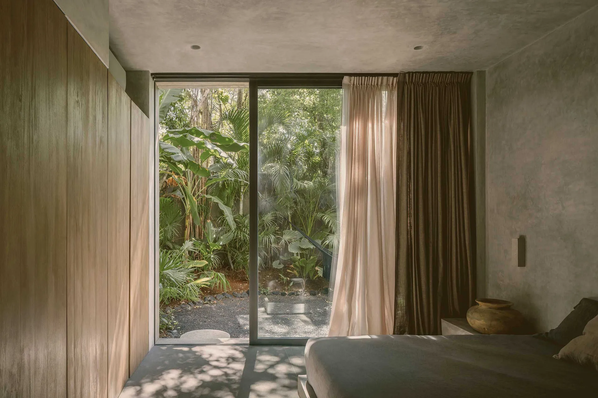 A modern bedroom with wooden panels, open curtains, and a view of greenery outside.