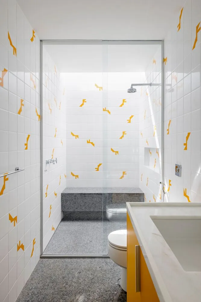 A minimalist bathroom with white tiles, a yellow cabinet, and a glass-enclosed shower.
