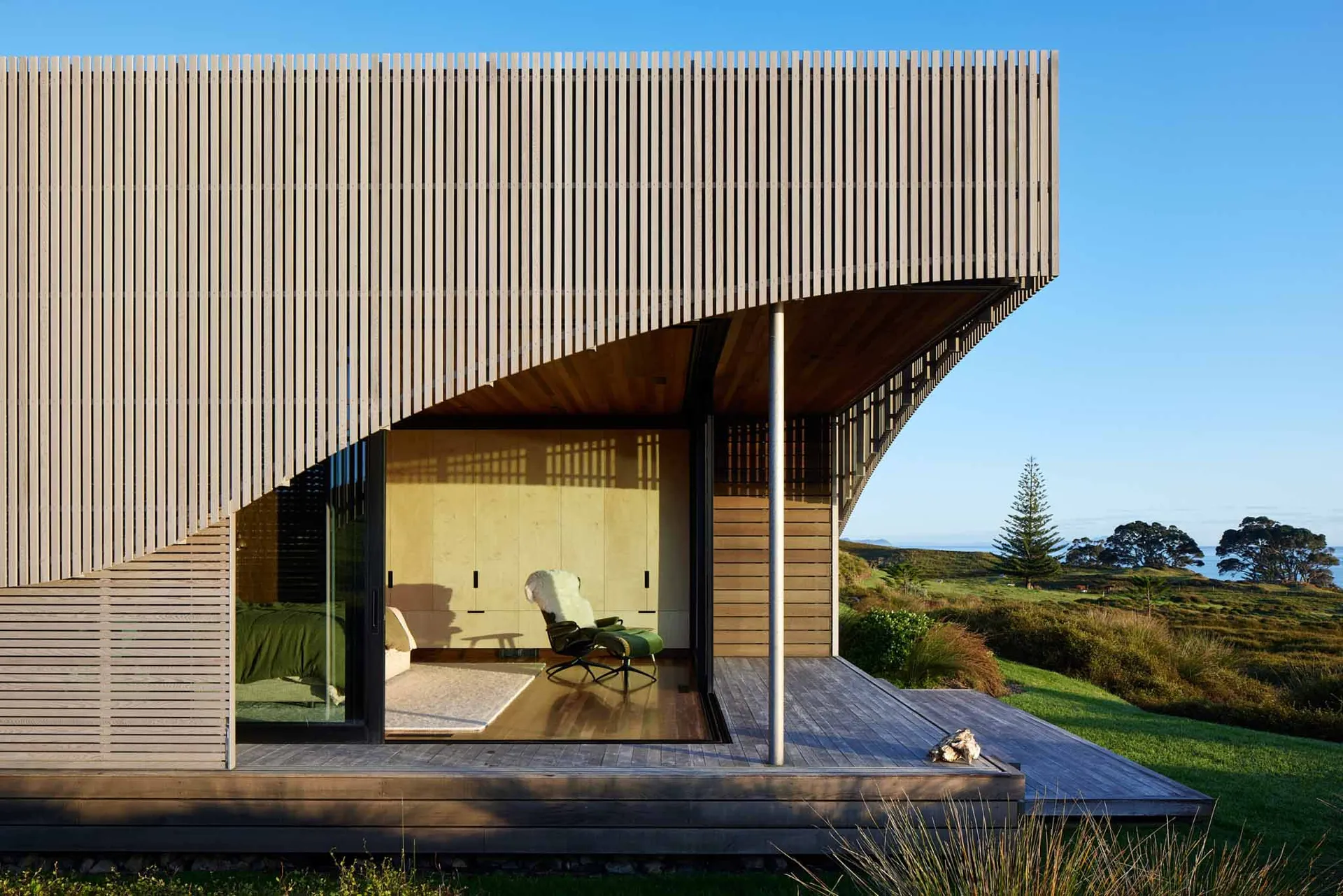 A modern, minimalist residential exterior featuring wood and glass materials, with a view of the surrounding landscape.