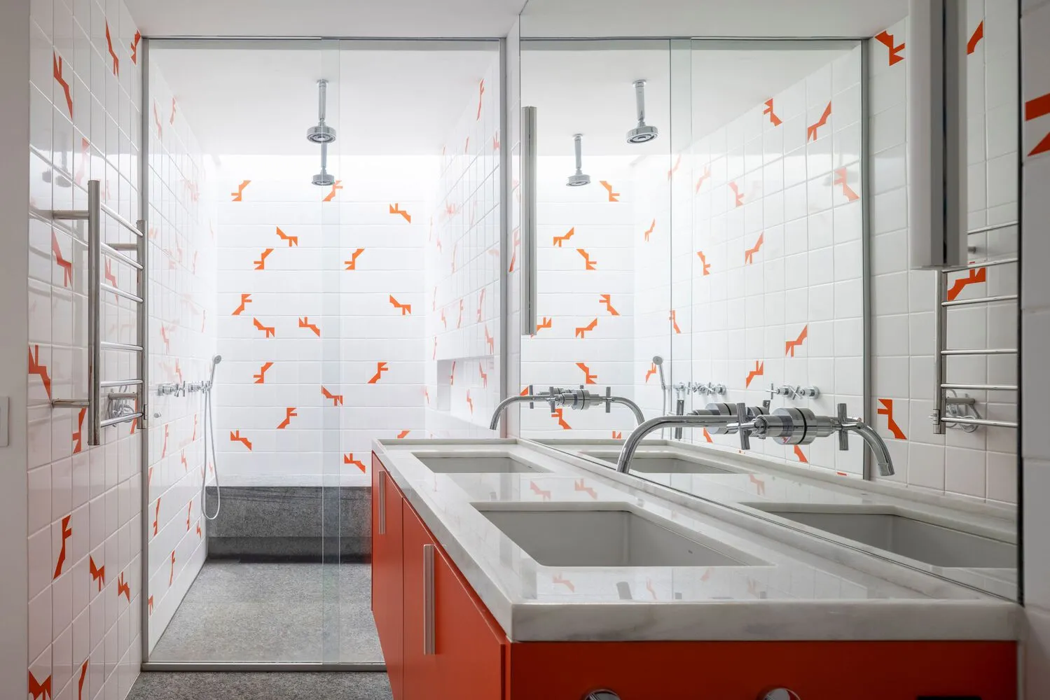 A modern bathroom with white and orange tiles, a double sink vanity, and a glass-enclosed shower.