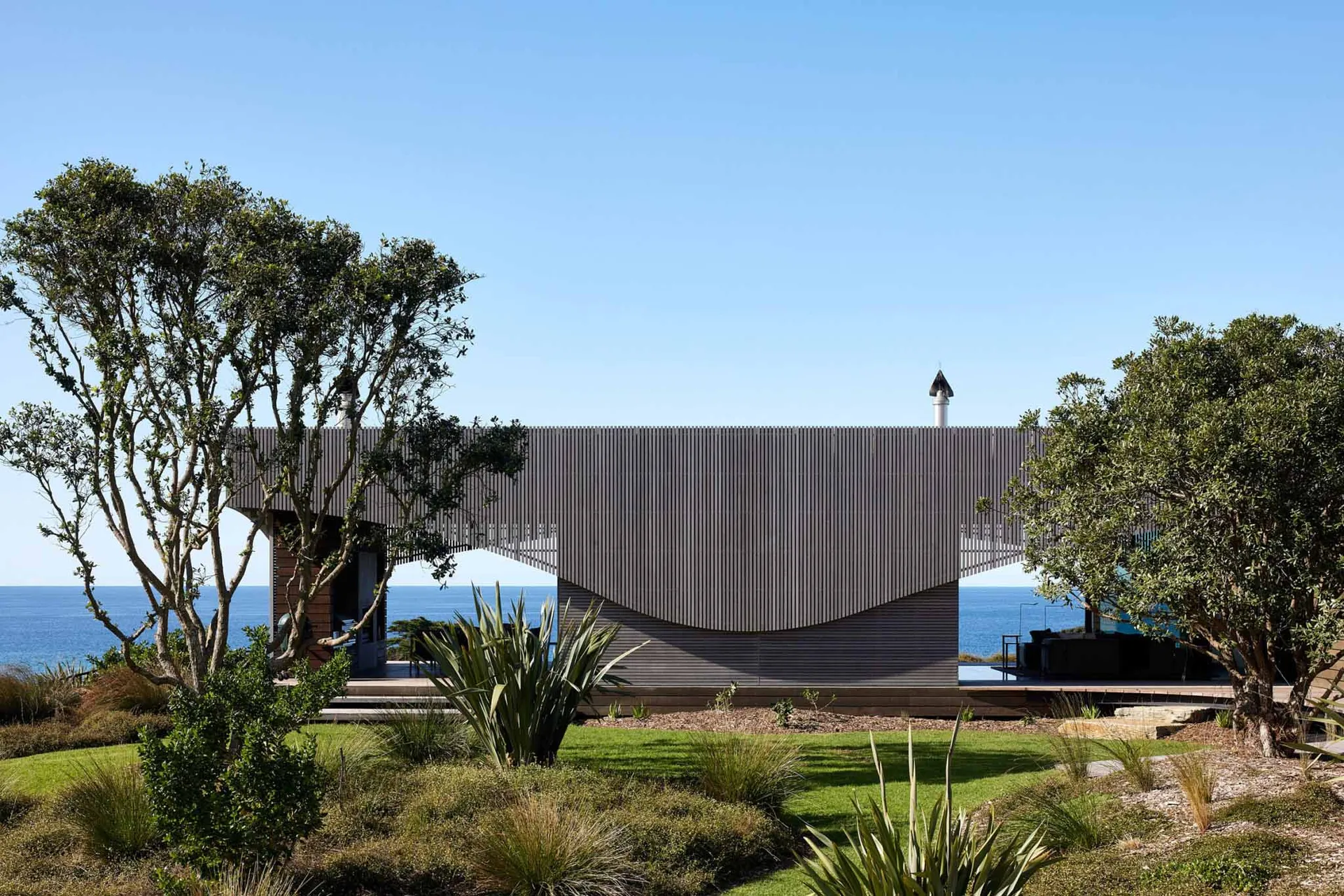 A modern house with a curved roof and concrete exterior walls sits on the coast.