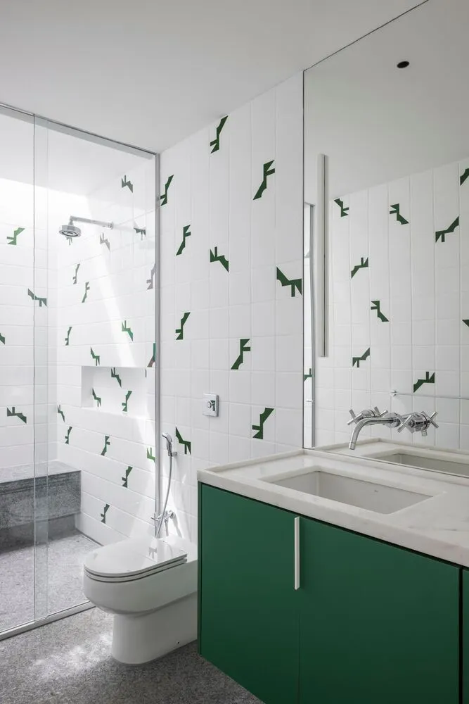 Minimalist bathroom with white walls adorned by green motif tiles, glass shower enclosure, and green cabinetry.