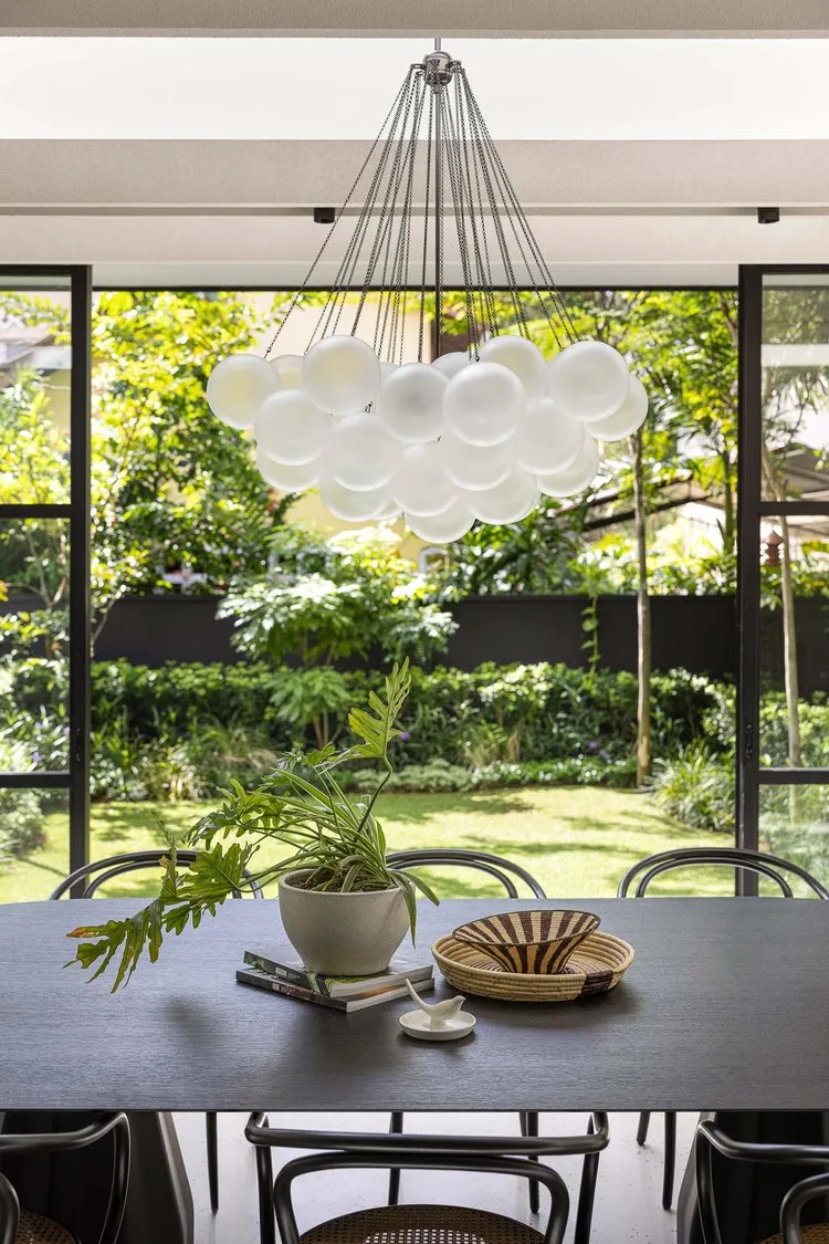 A minimalist dining room features a black table, black chairs, and a white round bubble chandelier hanging above the table wi