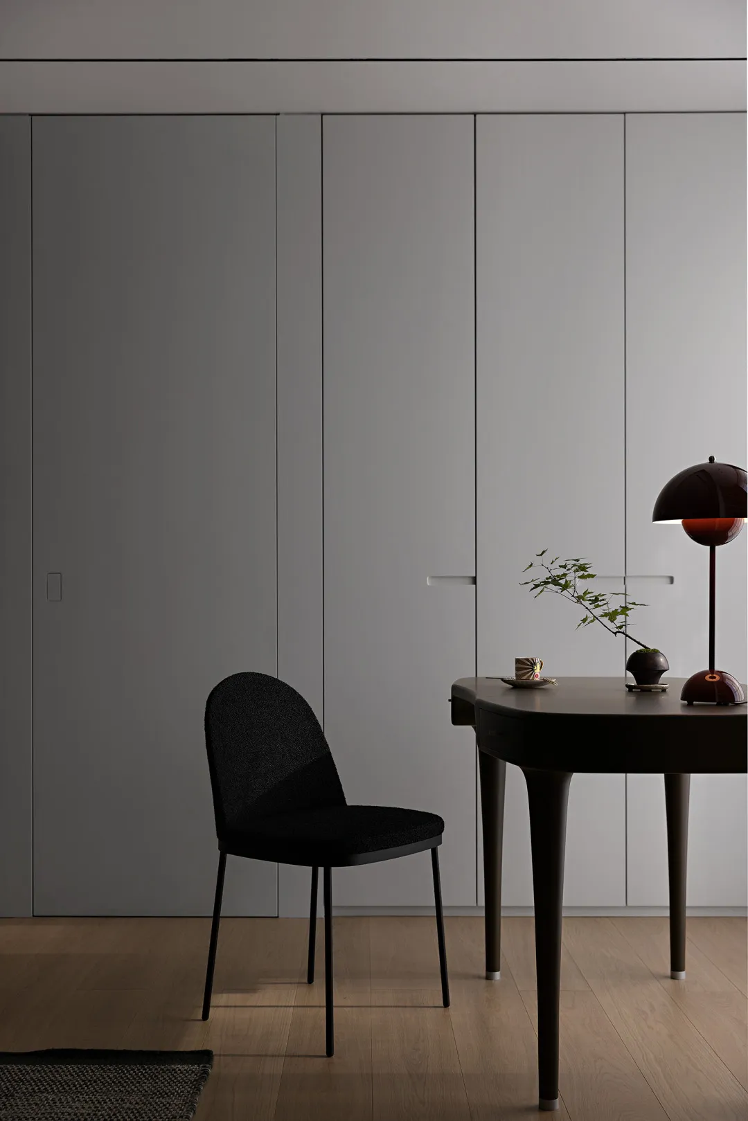 Minimalist office space featuring a black chair next to a minimalist desk with a lamp and a small plant.