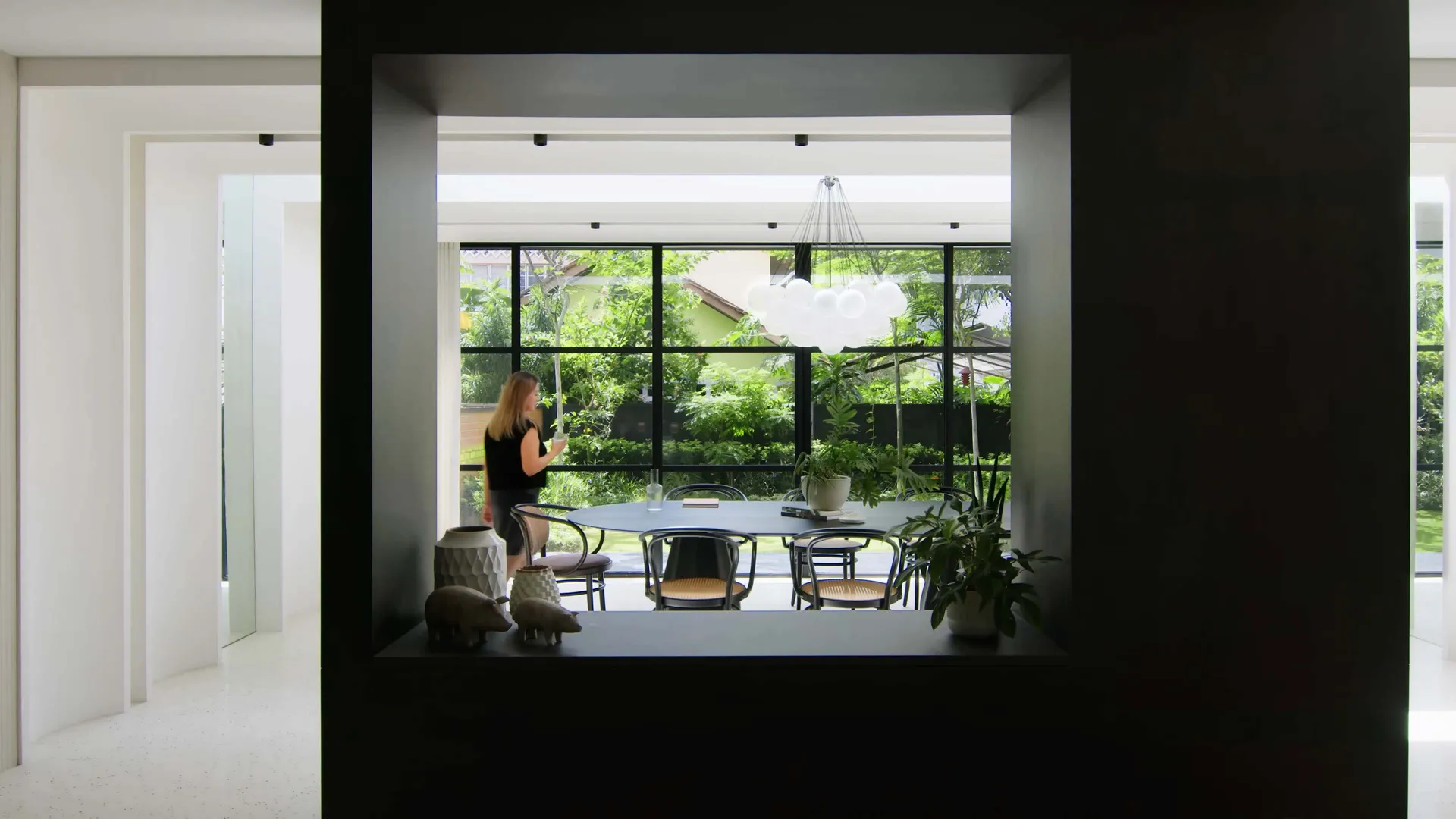 A modern dining room with a black metallic chandelier hanging above a table surrounded by chairs, featuring a minimalist desi